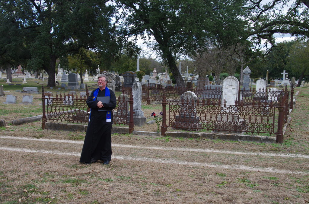 Saul, dressed in his clerical robe, stands in a cemetary